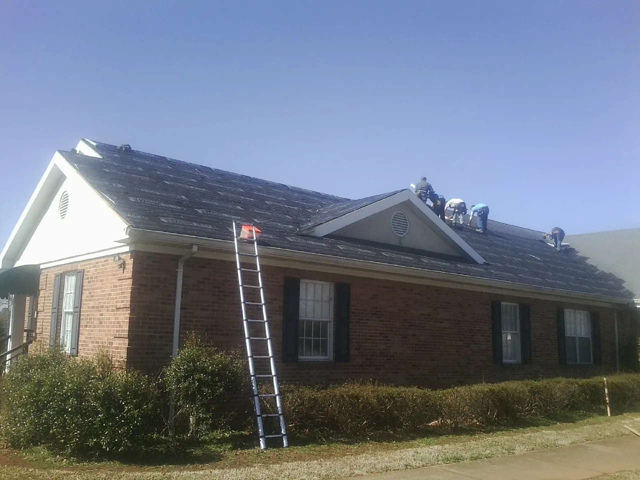 Crew tearing shingles off a brick ranch roof with a ladder set — Emergency Roof Repair work by our crew in Livermore Falls