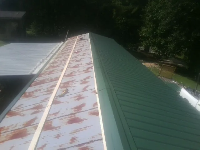 Old rusted panels beside newly installed green metal roofing — Wind Damage Roof Repair by Roofing Brothers in Livermore Falls