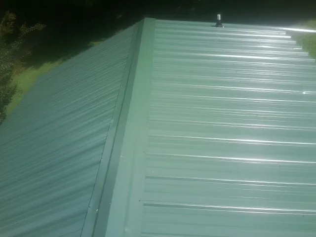 New green metal panels meeting at the ridge of a roof — Flat Roof Repair work by our crew in Livermore Falls