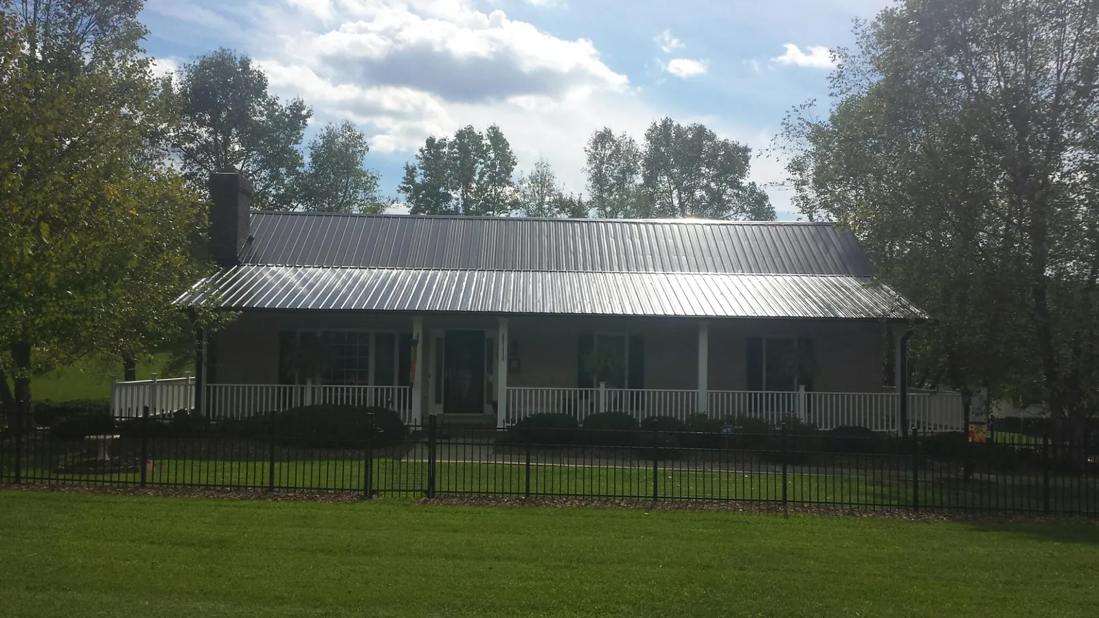 Gray metal roof on a brick ranch with a full width front porch — Gutter Guard Installation work by our crew in Livermore Falls