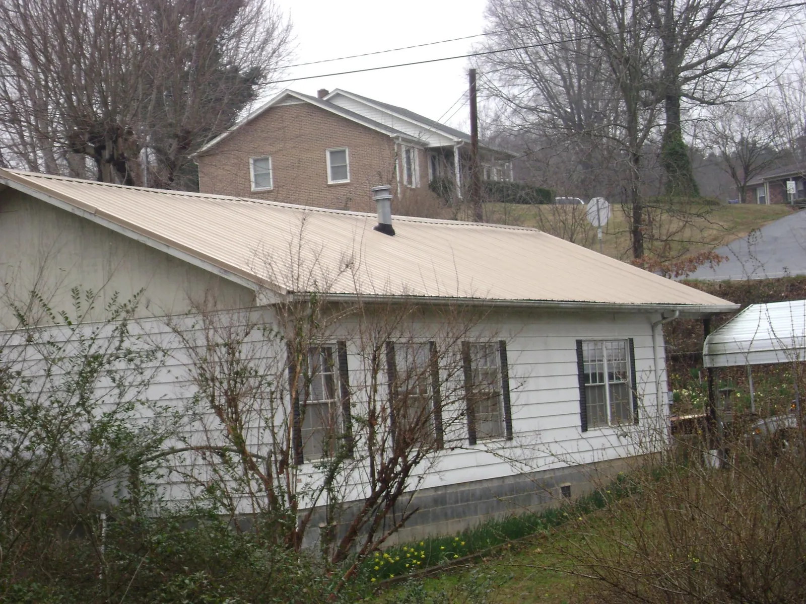 Tan metal roof on a white sided house set into a hillside — Commercial Roofing by Roofing Brothers in Livermore Falls