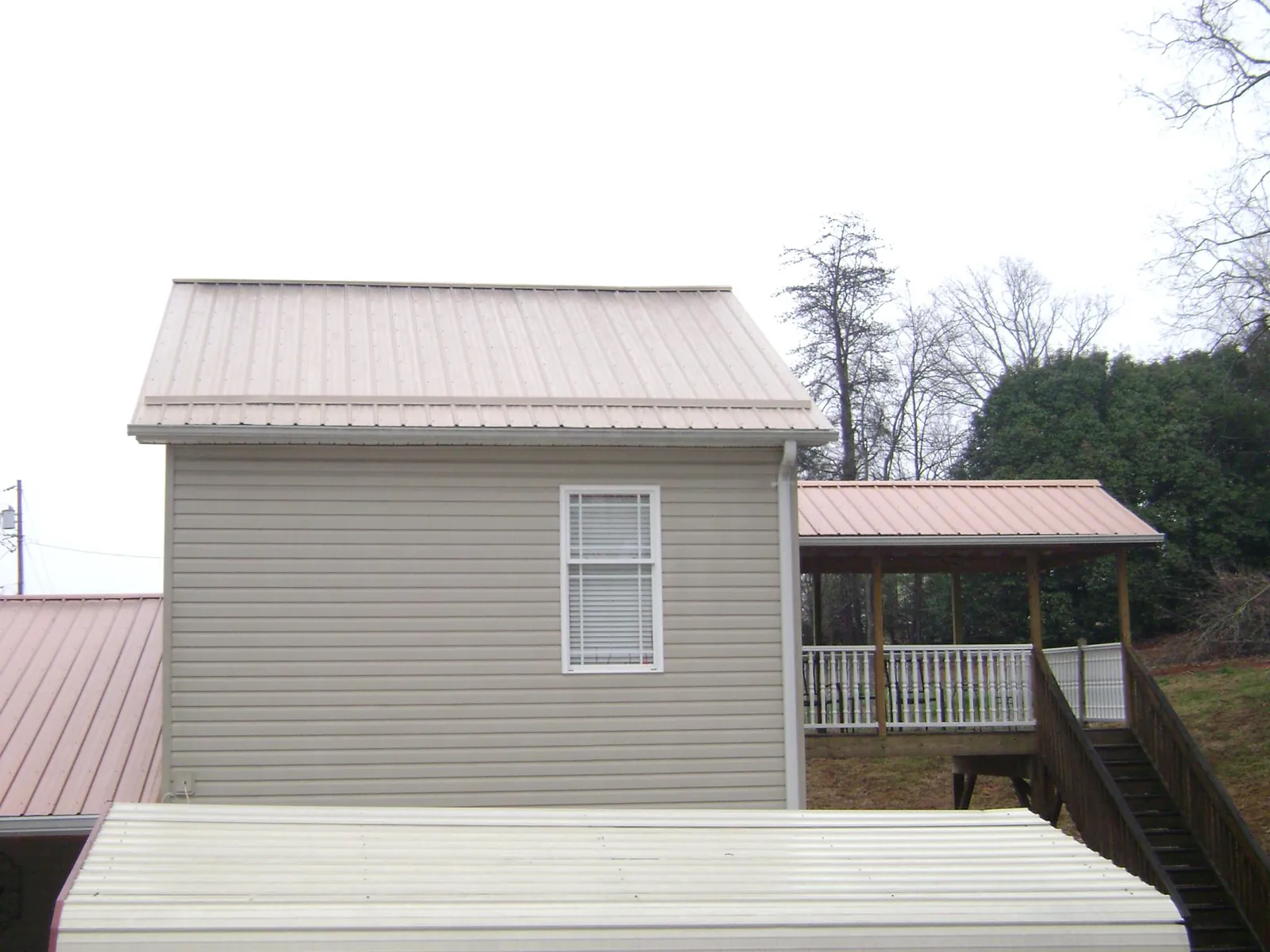 Tan metal roofs on a two story addition and attached porch, from a Roof Replacement job in Livermore Falls