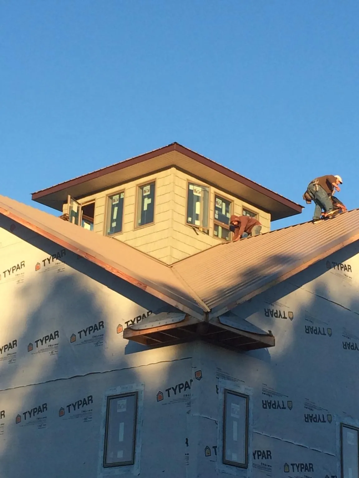 Roofers working around a rooftop cupola on a new metal roof at sunset — Roof Waterproofing in Livermore Falls by Roofing Brothers